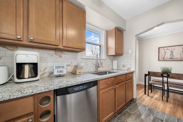 kitchen with stainless steel dishwasher, brown cabinetry, backsplash, and a sink