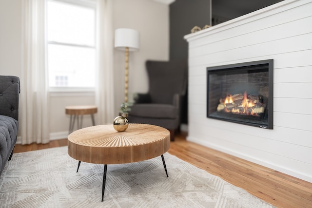 living area with a glass covered fireplace, baseboards, and wood finished floors