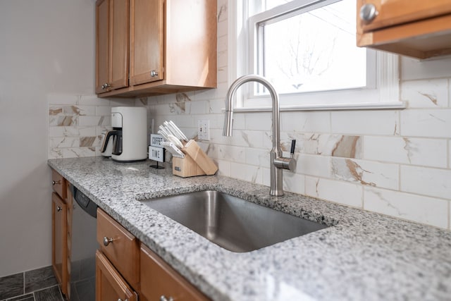 kitchen featuring a sink, light stone counters, stainless steel dishwasher, brown cabinetry, and decorative backsplash