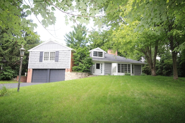 view of front of home featuring an attached garage, a chimney, aphalt driveway, and a front yard