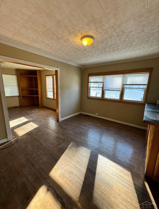 empty room with baseboards, wood finished floors, and crown molding