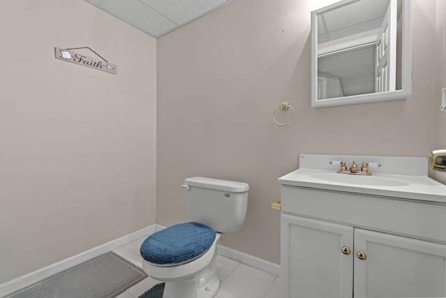 half bath featuring tile patterned floors, toilet, a drop ceiling, baseboards, and vanity