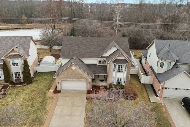 view of front facade featuring roof with shingles, concrete driveway, a front lawn, and fence