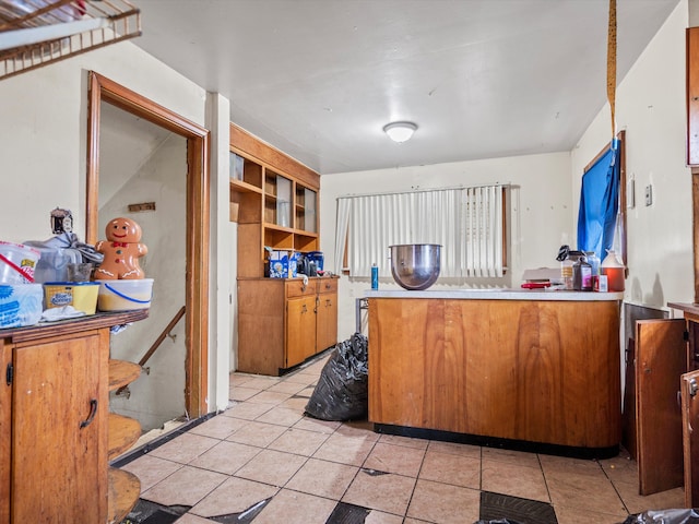 kitchen featuring a peninsula, light tile patterned floors, brown cabinetry, and light countertops