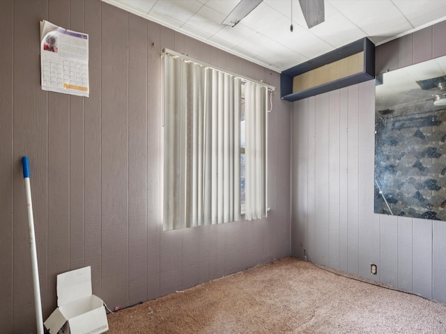 carpeted spare room featuring wood walls and a ceiling fan