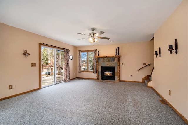 unfurnished living room featuring light colored carpet, a ceiling fan, a tile fireplace, baseboards, and stairs