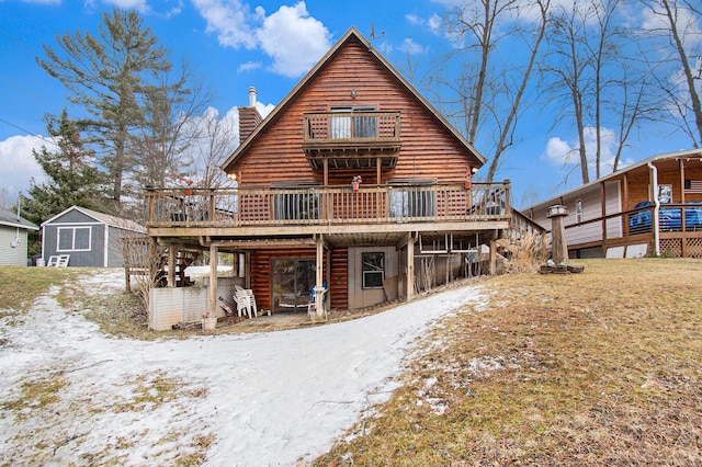 snow covered house with log exterior, a chimney, stairway, an outbuilding, and a wooden deck