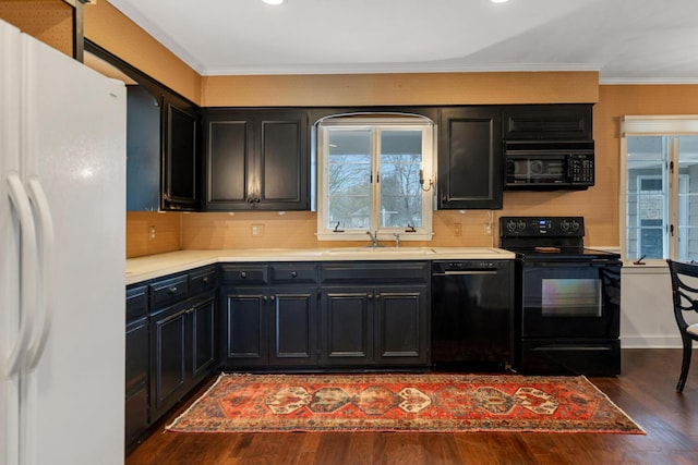 kitchen featuring wood finished floors, a sink, dark cabinetry, black appliances, and crown molding