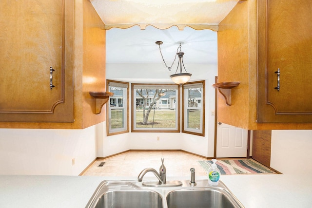 kitchen featuring a sink, visible vents, baseboards, light countertops, and brown cabinets