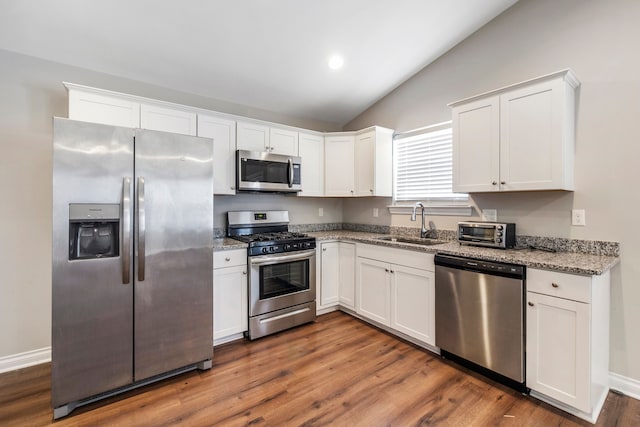 kitchen featuring light stone counters, vaulted ceiling, stainless steel appliances, white cabinetry, and a sink