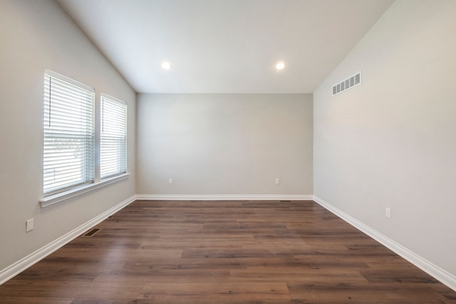 spare room featuring vaulted ceiling, dark wood-style flooring, visible vents, and baseboards