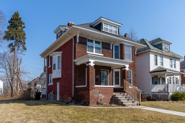 american foursquare style home featuring covered porch, brick siding, and a front lawn