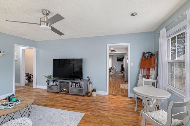 living area with a ceiling fan, a textured ceiling, baseboards, and wood finished floors