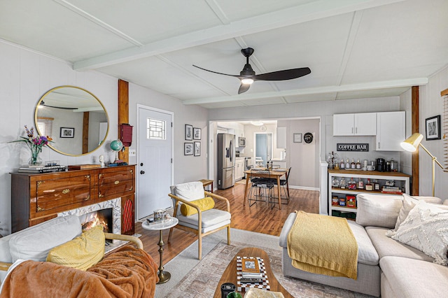 living room featuring a warm lit fireplace, beam ceiling, ceiling fan, and light wood finished floors