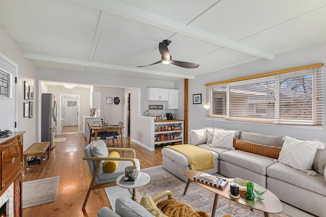 living area with light wood-style floors, beam ceiling, and a ceiling fan