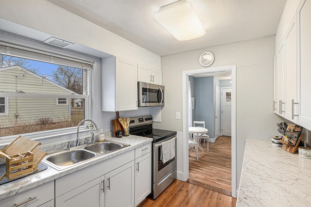 kitchen with stainless steel appliances, light countertops, a sink, and light wood-style flooring