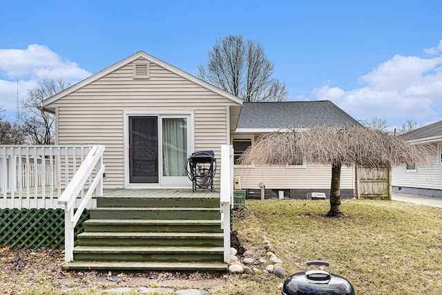 view of front of house featuring a shingled roof, a front yard, and a deck