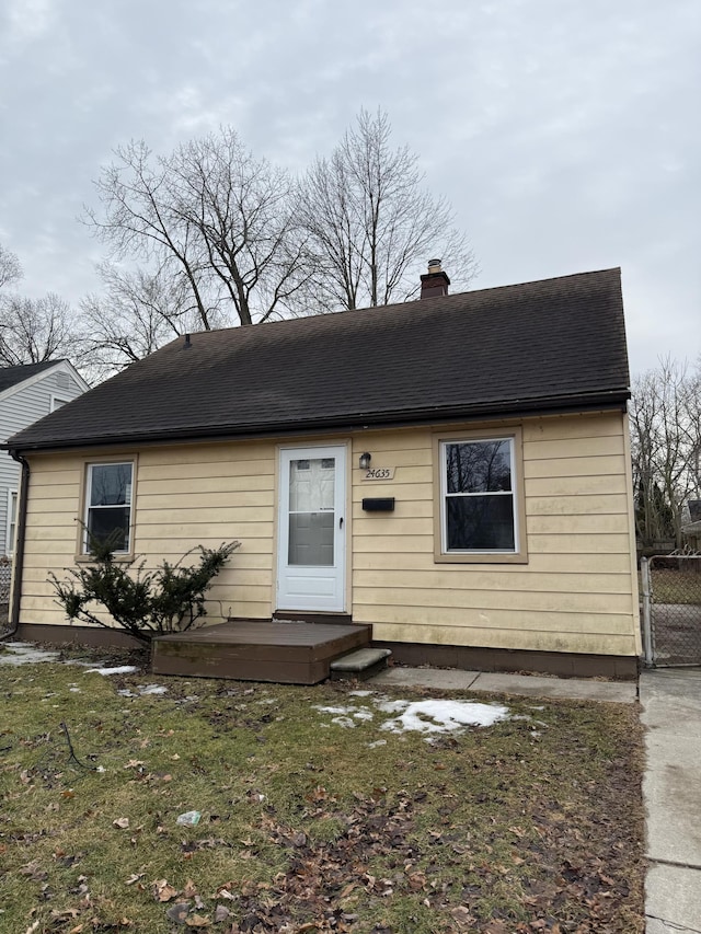 view of front of home featuring a shingled roof, a chimney, and a front yard