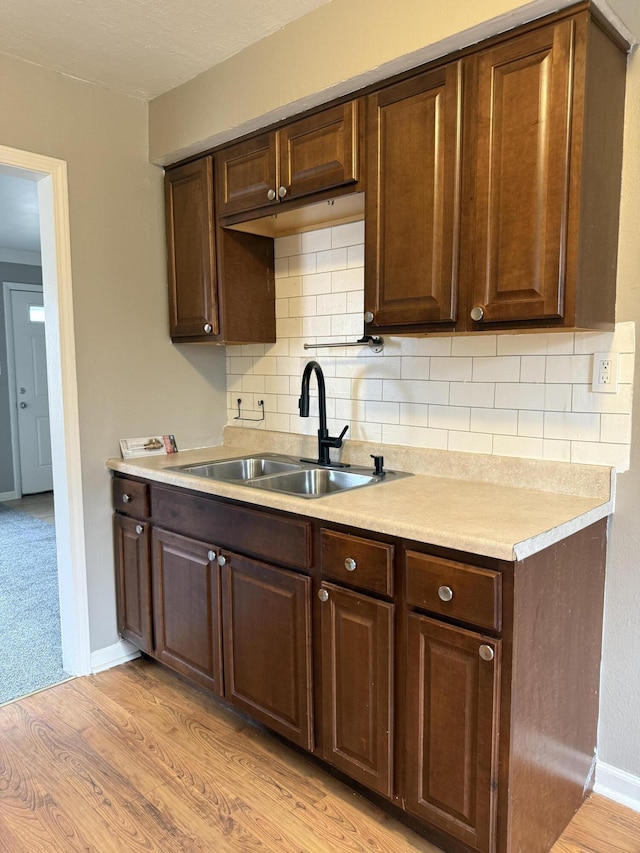 kitchen with dark brown cabinetry, light countertops, a sink, and light wood finished floors