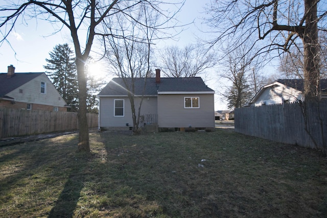 rear view of house with a shingled roof, a lawn, a chimney, and fence