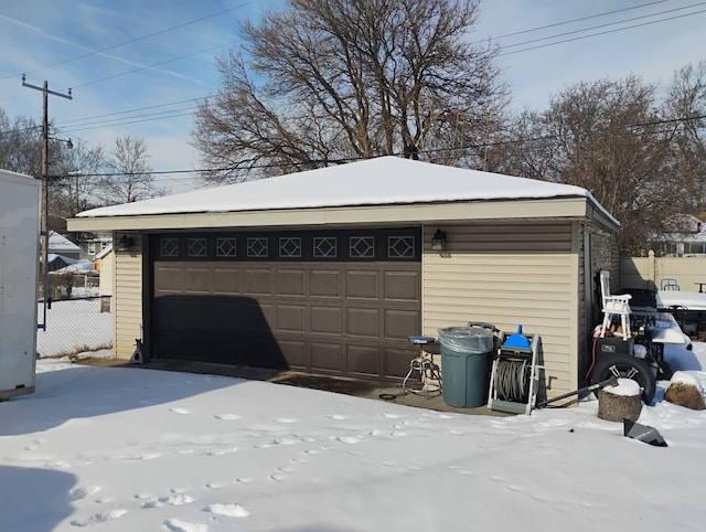 snow covered garage with fence and a garage