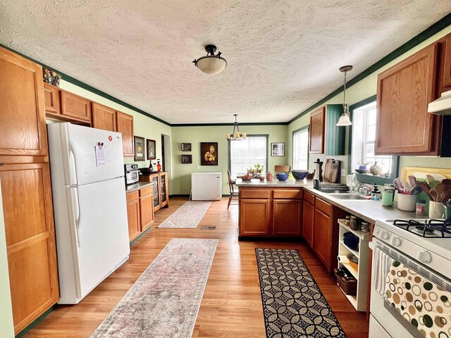 kitchen with hanging light fixtures, light wood-style floors, a sink, white appliances, and a peninsula