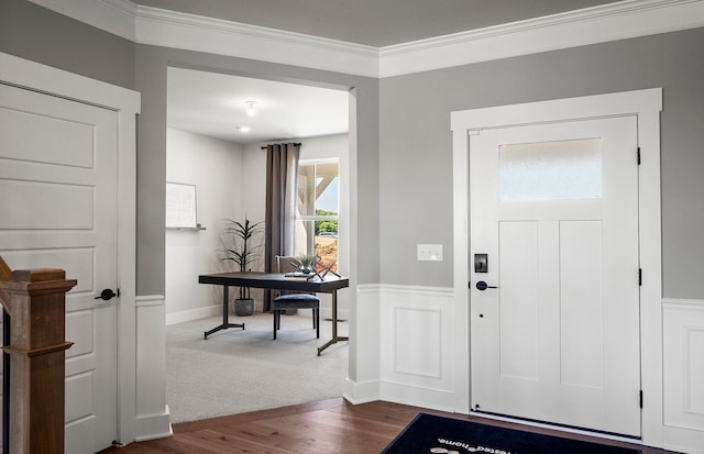 entrance foyer with ornamental molding, dark colored carpet, a wainscoted wall, and dark wood-type flooring