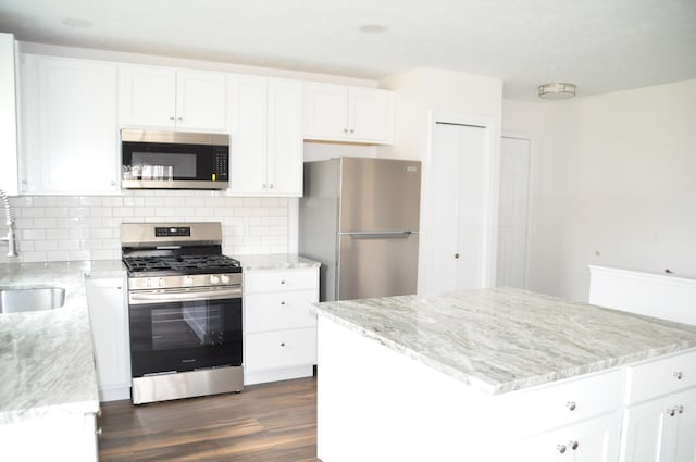 kitchen featuring tasteful backsplash, dark wood finished floors, appliances with stainless steel finishes, light stone countertops, and white cabinetry