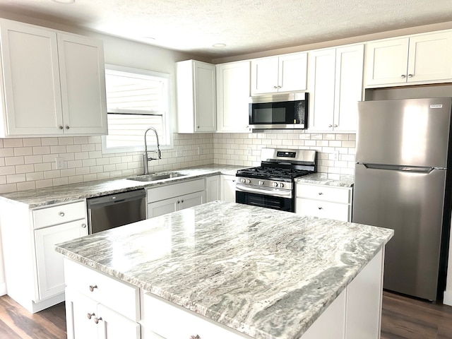 kitchen with dark wood-style flooring, a sink, white cabinetry, appliances with stainless steel finishes, and light stone countertops