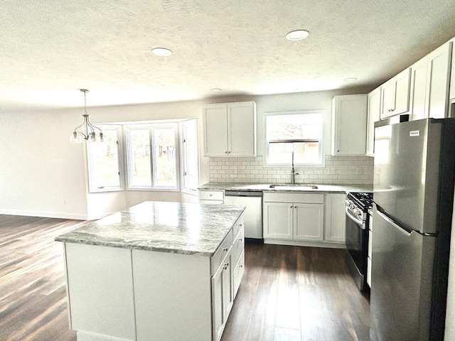 kitchen featuring light stone counters, dark wood finished floors, decorative backsplash, appliances with stainless steel finishes, and a sink