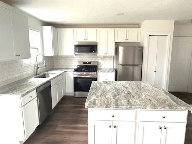 kitchen with light stone counters, stainless steel appliances, a kitchen island, a sink, and decorative backsplash