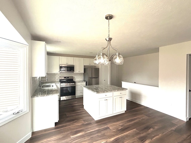 kitchen with white cabinets, a kitchen island, appliances with stainless steel finishes, dark wood-style flooring, and a sink