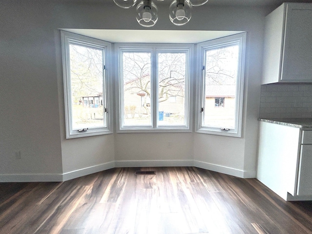 unfurnished dining area with dark wood-style floors, an inviting chandelier, visible vents, and baseboards