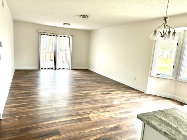 empty room featuring a textured ceiling, a chandelier, dark wood finished floors, and baseboards