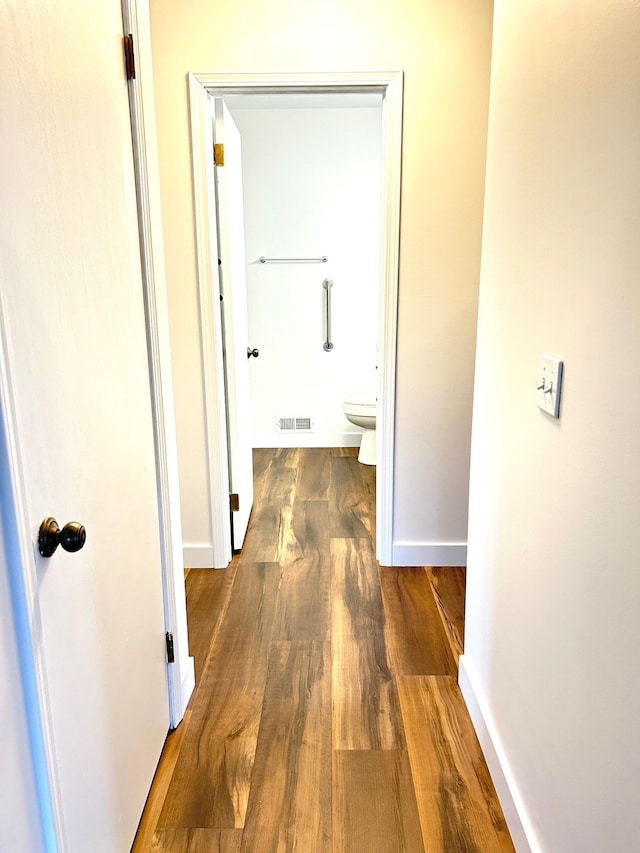 hall with visible vents, baseboards, and wood finished floors