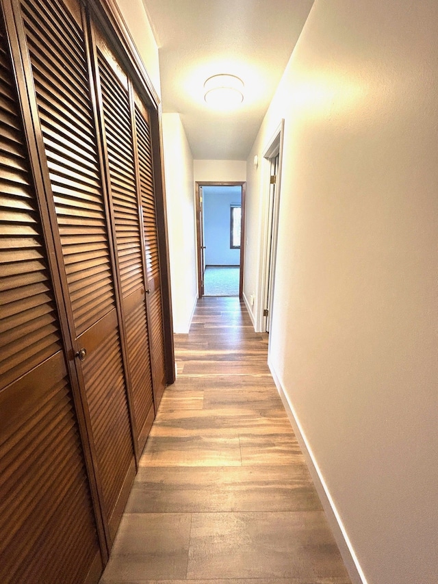 corridor featuring light wood finished floors and baseboards