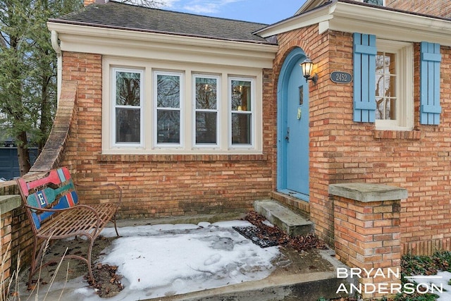 entrance to property featuring brick siding and roof with shingles