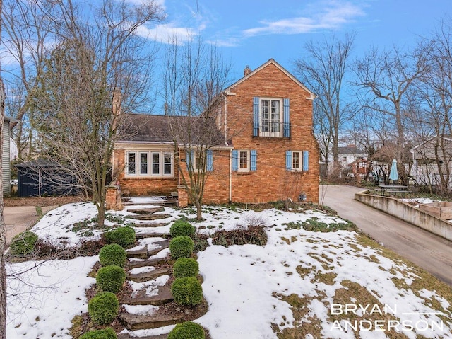 view of front of property featuring brick siding, driveway, and a chimney