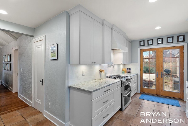 kitchen with light tile patterned floors, range with two ovens, white cabinetry, french doors, and decorative backsplash