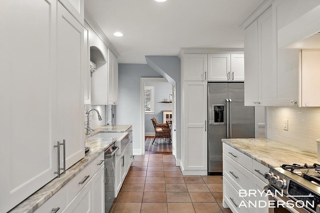 kitchen featuring light tile patterned flooring, white cabinets, appliances with stainless steel finishes, backsplash, and light stone countertops