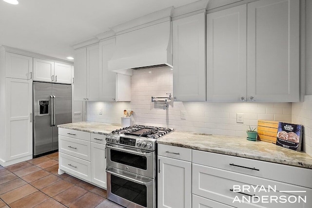 kitchen featuring custom range hood, appliances with stainless steel finishes, white cabinets, and decorative backsplash