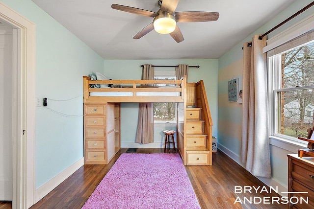 unfurnished bedroom featuring a ceiling fan, dark wood-style flooring, multiple windows, and baseboards