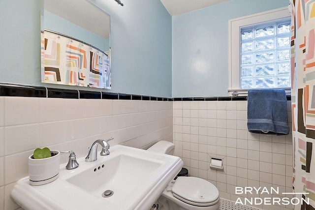 bathroom featuring a wainscoted wall, tile walls, toilet, a sink, and a shower with curtain