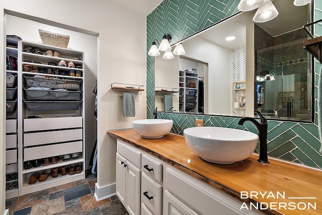 full bathroom featuring tasteful backsplash, a sink, stone tile flooring, and a walk in closet