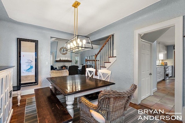 dining area featuring a chandelier, a textured wall, wood finished floors, baseboards, and stairs