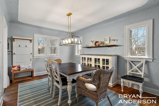 dining area with a notable chandelier, a textured wall, baseboards, and wood finished floors