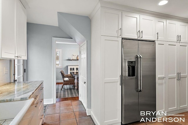 kitchen featuring light tile patterned floors, white cabinets, light stone countertops, stainless steel refrigerator with ice dispenser, and a sink