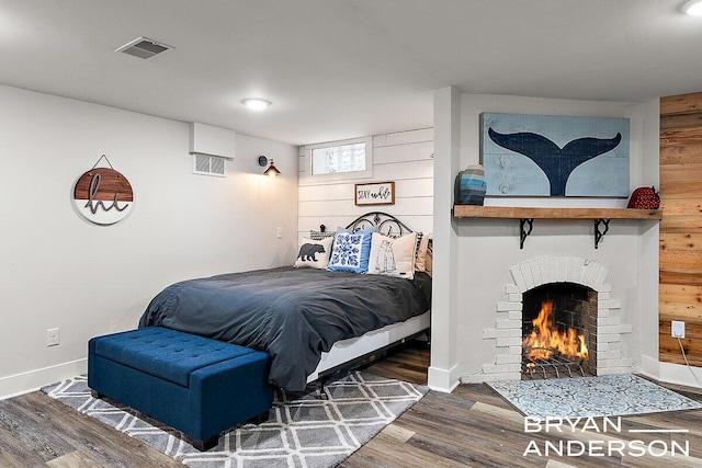 bedroom with visible vents, a fireplace, baseboards, and wood finished floors