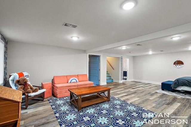 living room featuring stairway, baseboards, visible vents, and wood finished floors