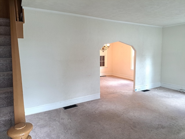 carpeted empty room with visible vents, arched walkways, baseboards, stairway, and ornamental molding